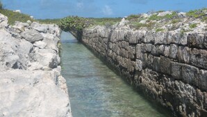 Un canal de piedra estrecho con agua cristalina, rodeado de terreno rocoso y vegetación escasa.