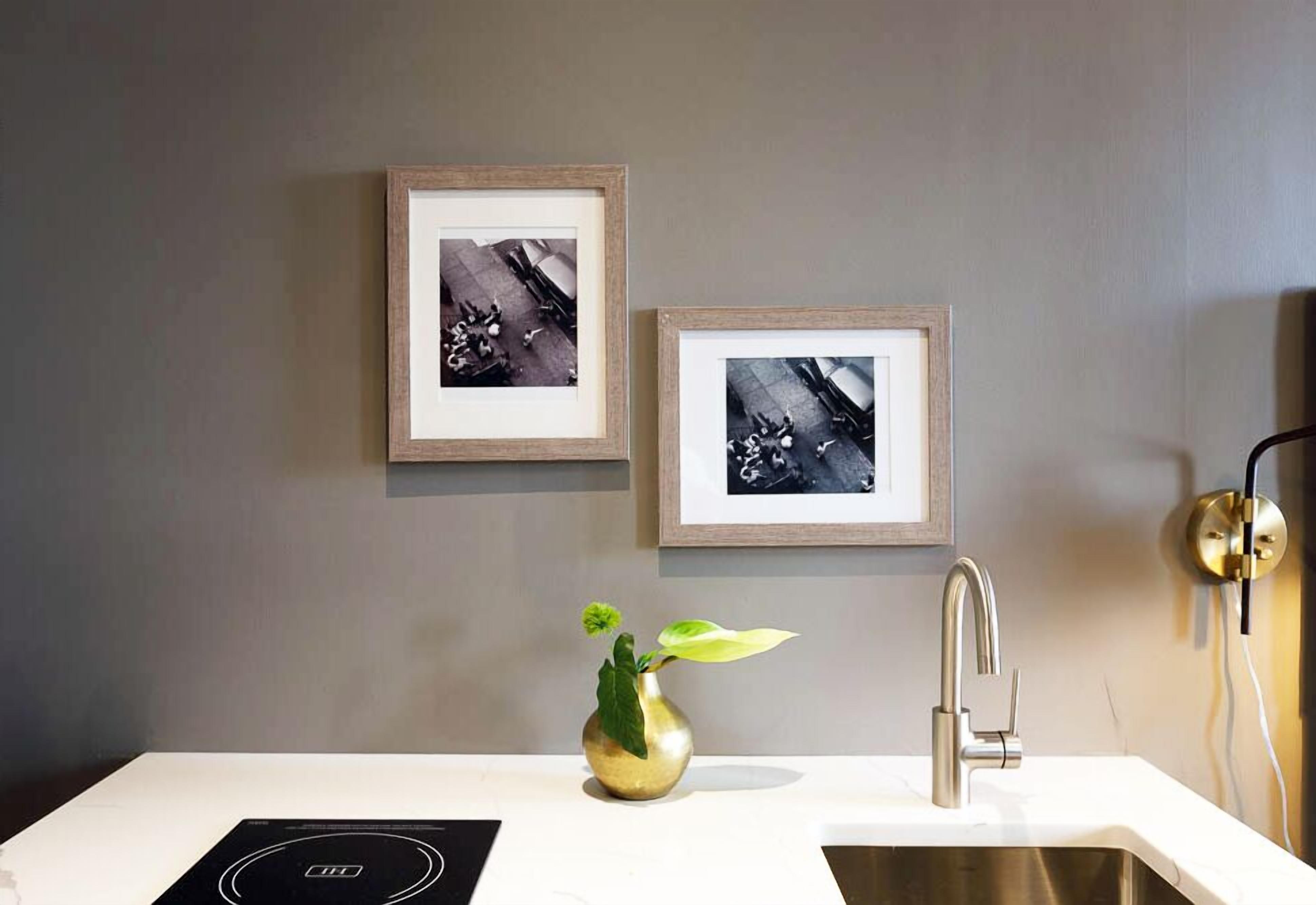Une salle de bain moderne avec un lavabo blanc, un vase doré orné d’une plante et deux photographies encadrées accrochées au mur.