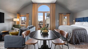Une chambre d’hôtel moderne dot ée d’un grand lit, d’une table à manger avec des chaises, d’un canapé et offrant une vue sur la ville grâce à de grandes fenêtres.