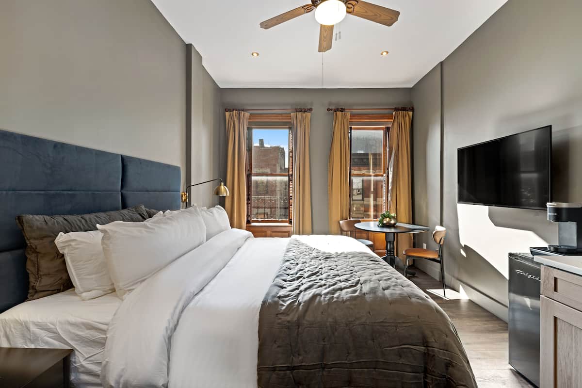 Een moderne hotelkamer met een groot bed, een plafondventilator, een televisie en een kitchenette.