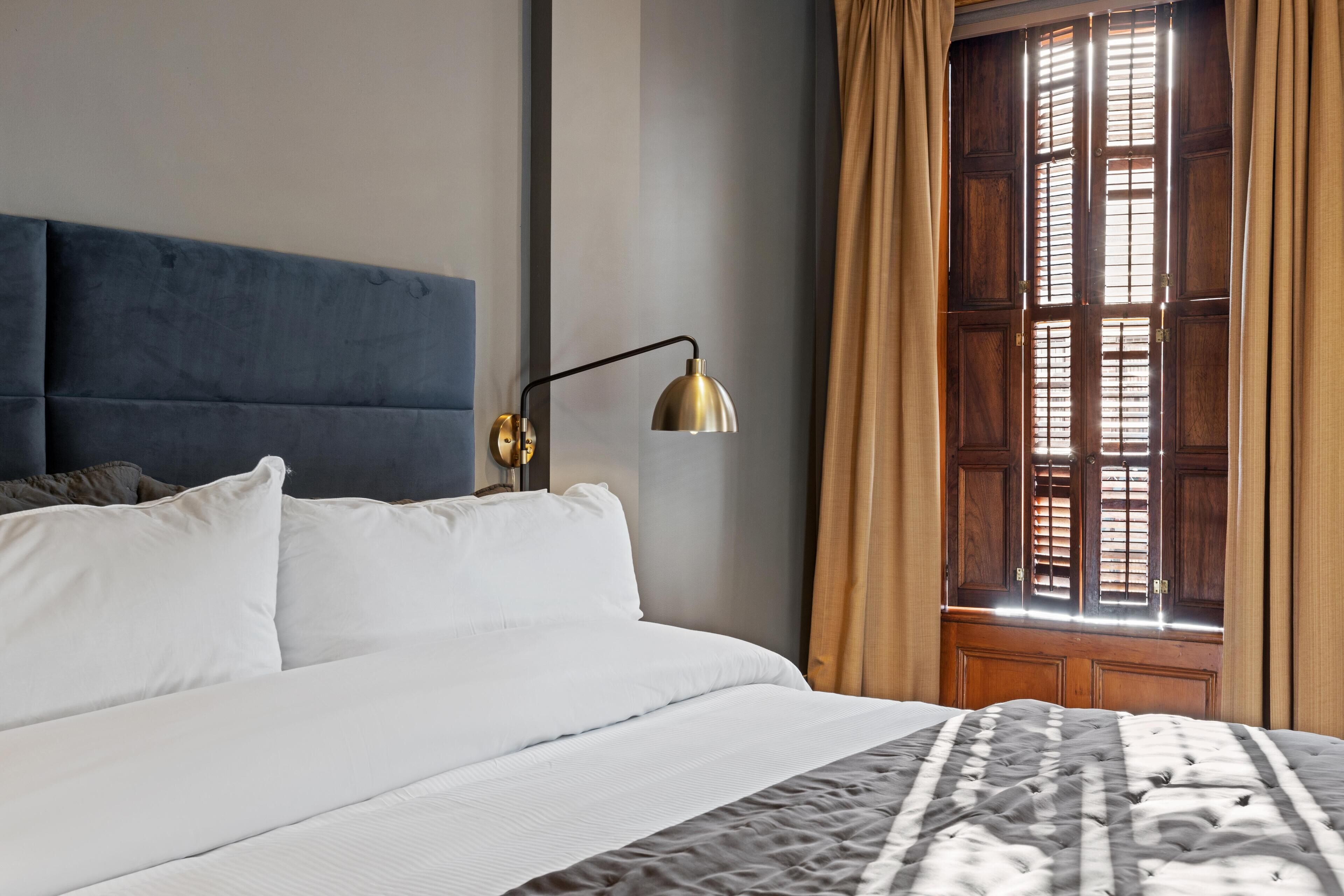 A neatly made bed with white linens, a dark blue headboard, and a patterned throw blanket.