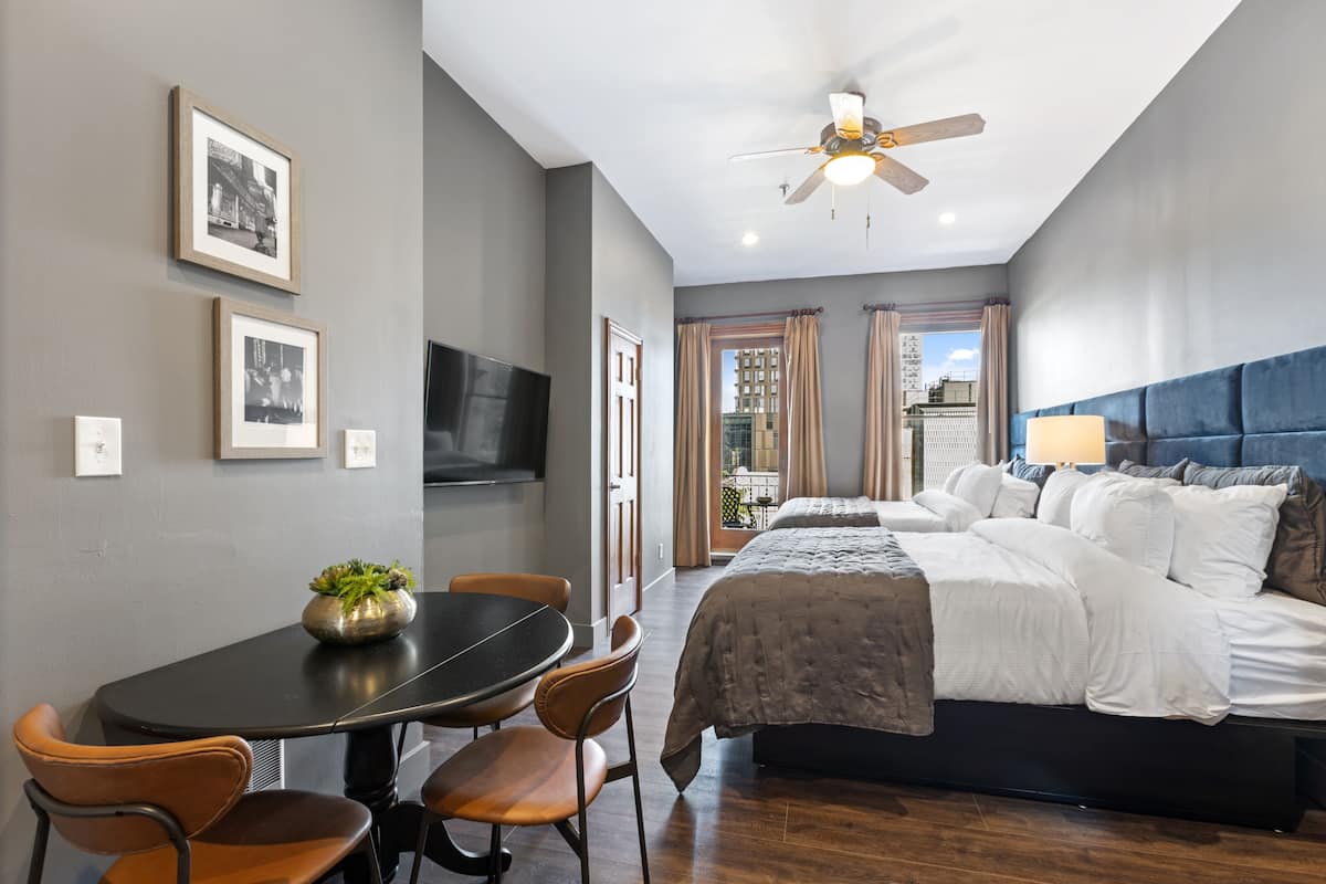 Een moderne slaapkamer met een bed, een eettafel met stoelen, een plafondventilator en ingelijste foto's aan de muur.