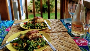 A dining table with two plates of food and a bottle of wine on a woven tablecloth.