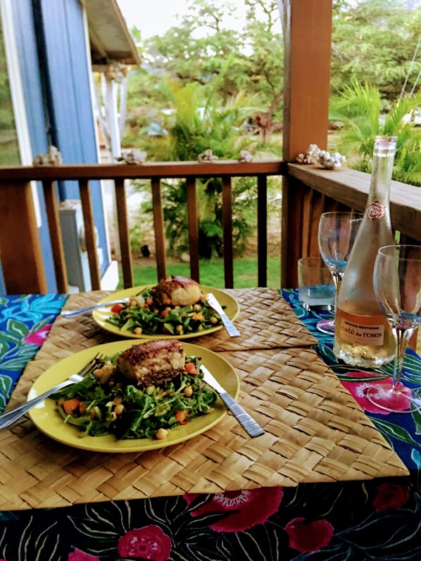 A dining table with two plates of food and a bottle of wine on a woven tablecloth.