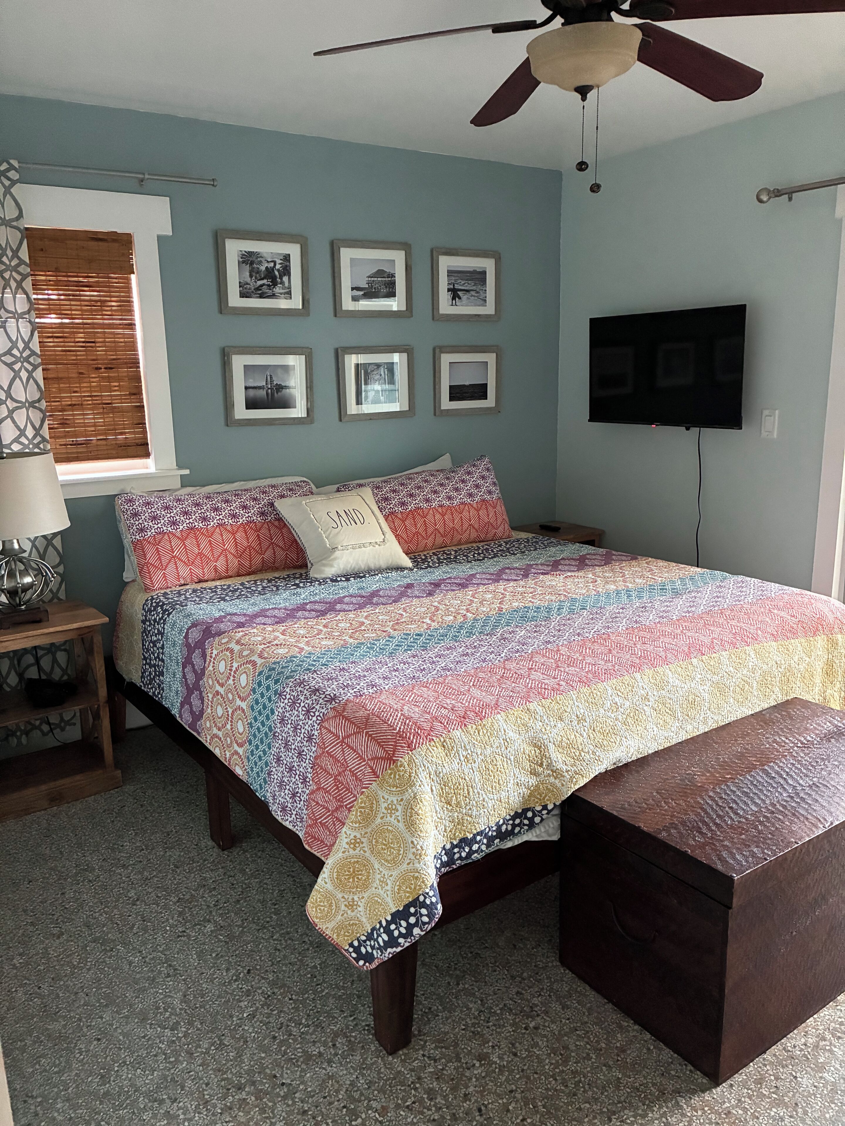 Een slaapkamer met een bed, een plafondventilator, een televisie en ingelijste foto's aan de muur.