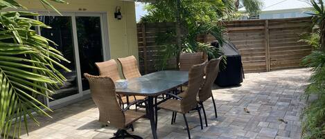 An outdoor patio with a table and chairs, surrounded by palm trees and a wooden fence.