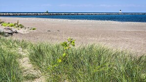 Une plage dotée d’une digue rocheuse, d’un phare et d’un rivage sablonneux où la végétation est clairsemée.