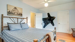 Une chambre à coucher avec un lit, un ventilateur de plafond, une sculpture d’ours fixée au mur et une porte.