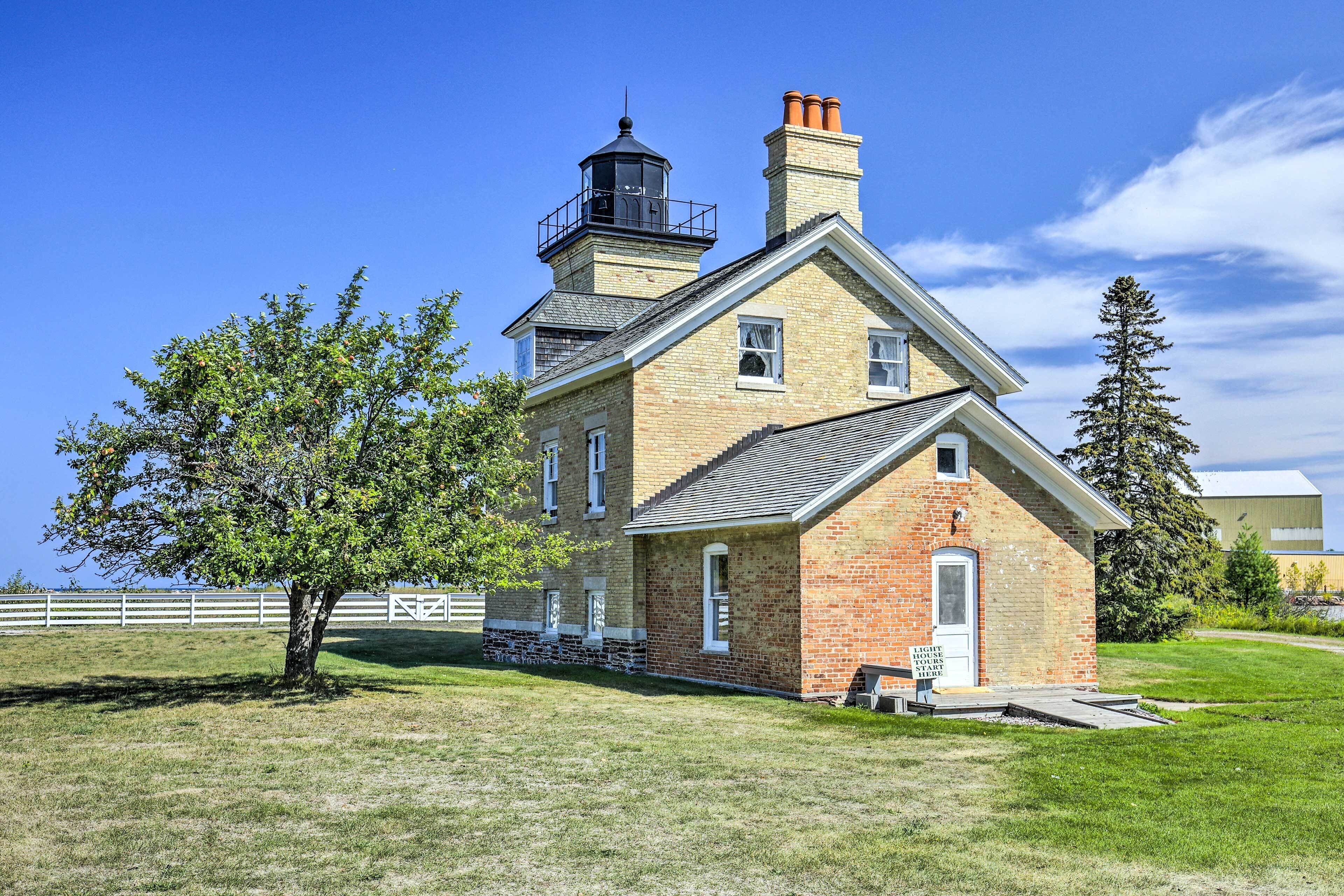 Un edificio storico in mattoni con una torre imponente e una piccola struttura adiacente con la scritta 'Light House Tours Start Here'.