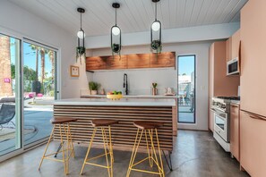 Une cuisine moderne dotée d’un îlot central, de tabourets de bar, de plantes suspendues et offrant une vue sur l’extérieur.