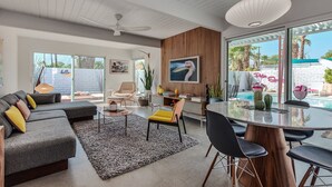 A modern living room with a sectional sofa, a dining table, and a view of a swimming pool. - Dreamy Mid Century Modern House with Saltwater Pool &  Resort Style Backyard (Palm Springs)