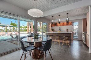 Une cuisine moderne dotée d’un îlot central, d’un coin repas avec une table ronde et des chaises, et offrant une vue sur une piscine à l’extérieur.