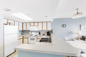 Kitchen features a central island with a sink and stove, light-colored cabinetry, and a white countertop.