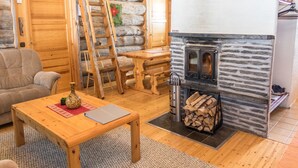 Un acogedor interior de cabaña de troncos con chimenea de piedra, muebles de madera y una escalera.