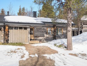 Una cabaña de troncos con terraza de madera, un porche cubierto y un paisaje cubierto de nieve.