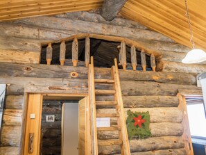 A wooden interior with a ladder leading to a loft area, a door, and a wall-mounted light fixture.
