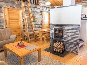 A cozy log cabin interior with a wooden table, a sofa, a fireplace, and a ladder.