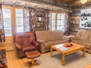 A cozy log cabin interior with a leather armchair, a brown sofa, and a wooden coffee table.