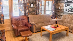 Un interior acogedor de cabaña de madera con un sillón de cuero, un sofá marrón y una mesa de centro de madera.