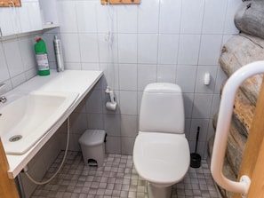 Un baño con lavamanos blanco, inodoro y un pequeño cubo de basura. Hay dos botellas sobre el mostrador del lavamanos.
