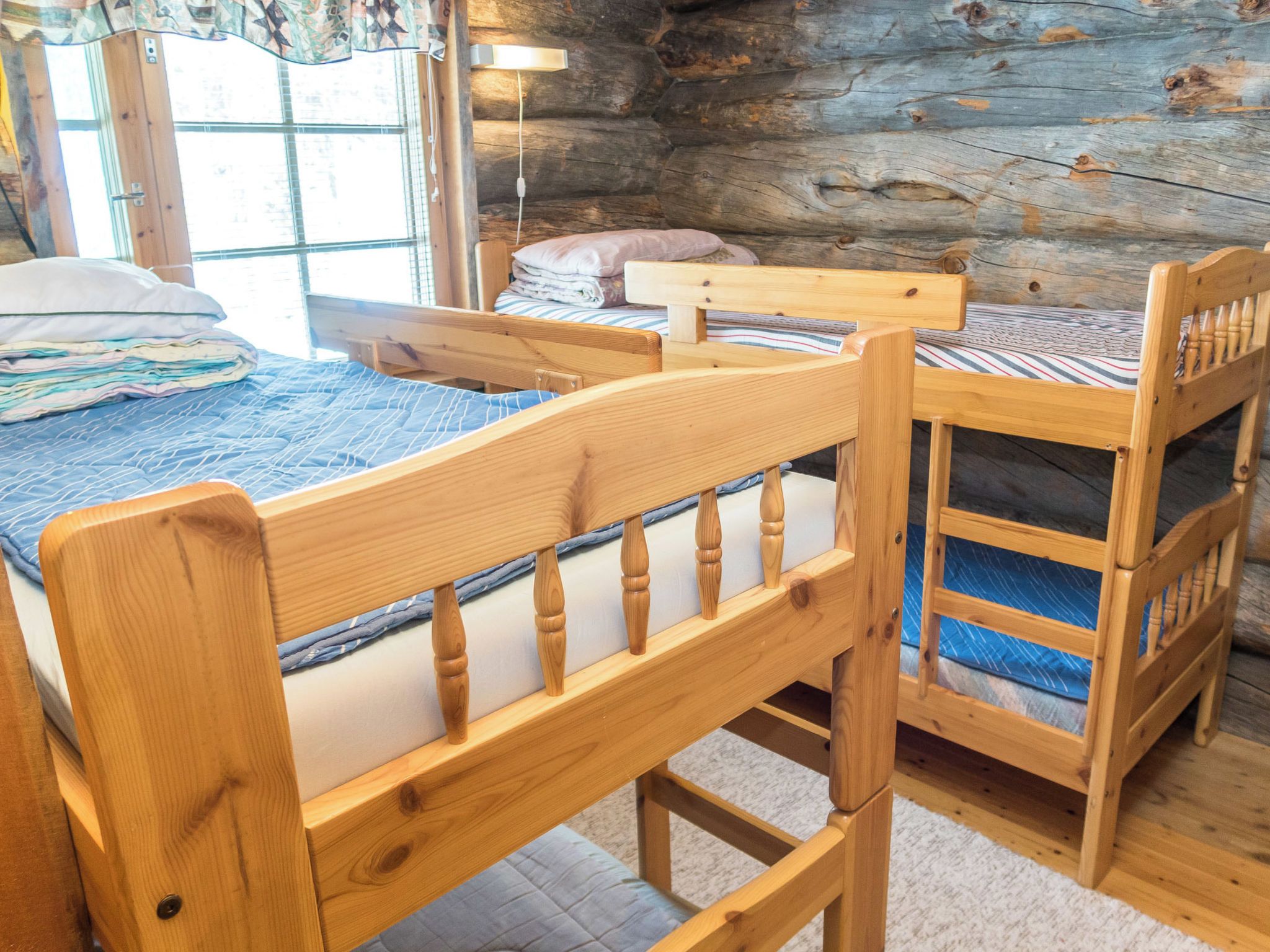 A wooden bunk bed with a headboard and footboard, a small wooden table, and a window with curtains.