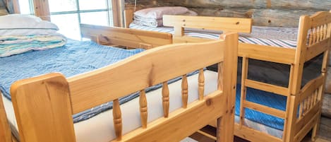 A wooden bunk bed with a headboard and footboard, a small wooden table, and a window with curtains.