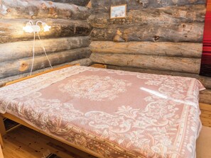 A wooden log cabin interior with a bed, a framed picture on the wall, and a power outlet.