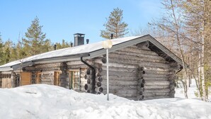 Una cabaña de troncos con techo cubierto de nieve, puertas de madera y una chimenea.