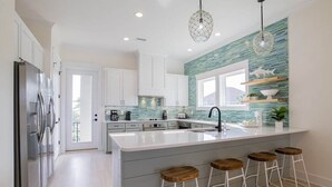 Una cocina moderna con una isla grande, armarios blancos y una salpicadura trasera color turquesa.
