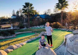 Ein Golfplatz mit Putting Green, Teich und einem Haus im Hintergrund.