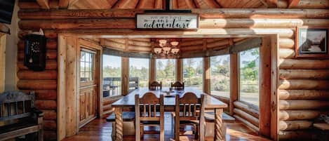 A log cabin interior with a dining table, chairs, a clock, and a sign that reads 'we are living adventure.'