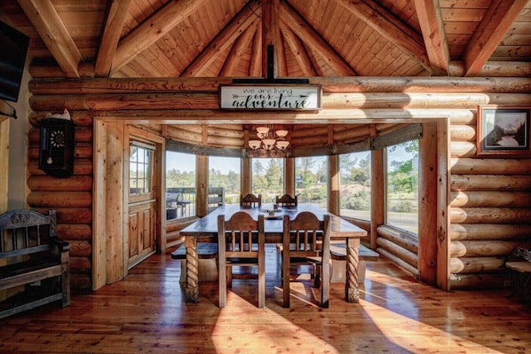 A log cabin interior with a dining table, chairs, a clock, and a sign that reads 'we are living adventure.'