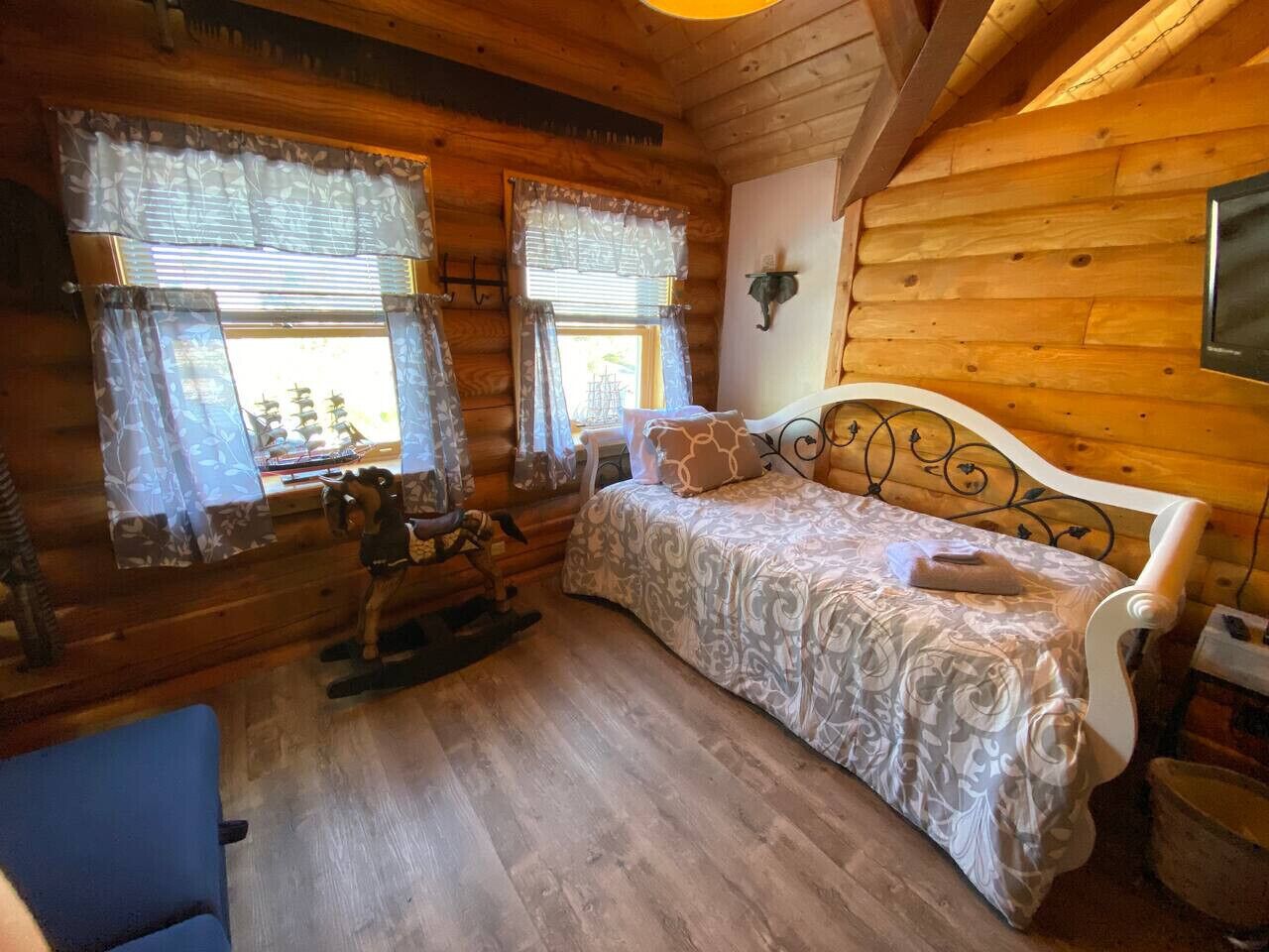 A wooden cabin room with a bed, rocking horse, and a small table.