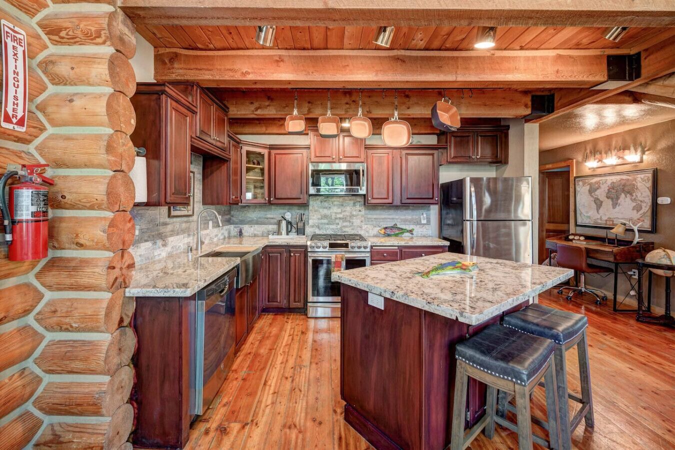 A log cabin-style kitchen with a stone wall, wooden cabinets, a stainless steel refrigerator, and a granite countertop.