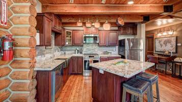 A log cabin-style kitchen with a stone wall, wooden cabinets, a stainless steel refrigerator, and a granite countertop.
