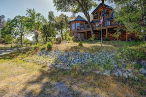 A log cabin with a stone foundation, surrounded by a natural landscape with trees and a stone wall.