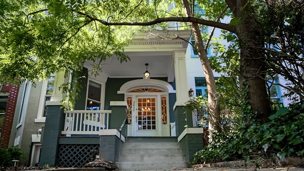 A two-story house with a porch, a white door, and a small staircase leading to the entrance.