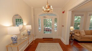 A hallway with a chandelier, a mirror, a console table with lamps, a sofa, and a rug.