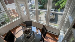 A dining area with a glass table, black chairs, and a view of the street through large windows.