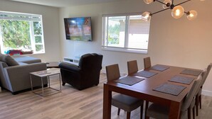En moderne stue med sofa, spisebord med stole, et TV ophængt på væggen og en lysekrone.