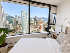 A bedroom with a large window, a telescope, a bed, and a potted plant.