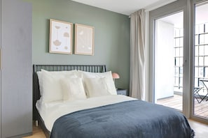Quarto com cama, mesa de cabeceira, luminária e duas pinturas abstratas emolduradas na parede.