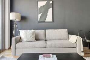 A modern living room with a grey sofa, a floor lamp, and a framed abstract painting on the wall. - Chic Wieden 1BR w/ Balcony, Gym, Elevator, walk to U-Bahn, by Blueground (Vienna)