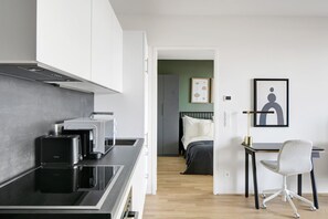 A modern kitchen with a built-in stove, toaster, and coffee maker. A bed with white bedding and a green wall is visible in the adjacent room. - Chic Wieden 1BR w/ Balcony, Gym, Elevator, walk to U-Bahn, by Blueground (Vienna)