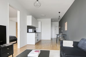 A modern living room with a black sofa, a coffee table with a book, a TV, and a kitchen area in the background. - Lovely Wieden 1BR w/ Balcony, Gym, Elevator, walk to U-Bahn, by Blueground (Vienna)