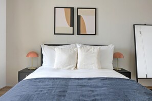 A neatly made bed with white linens and two pillows, flanked by two bedside tables with lamps, in a room with a plain wall and a door. - Lovely Wieden 1BR w/ Balcony, Gym, Elevator, walk to U-Bahn, by Blueground (Vienna)