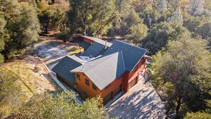 A two-story house with a sloped roof, surrounded by trees and a dirt path. - The Red Oasis (Oakhurst)