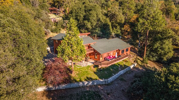 A large, two-story wooden house with a balcony, surrounded by dense forest. - The Red Oasis (Oakhurst)