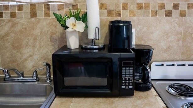 A kitchen with a black microwave, a coffee maker, and a sink. - 
5 min drive to Junkanoo Beach, Arawak Cay, Ardastra Garden & Zoo & Attractions (Nassau)