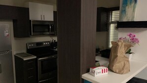 Une cuisine avec des meubles de couleur sombre, un four à micro-ondes, une cuisinière et une boîte de KFC posée sur le comptoir.